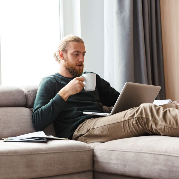 Man ontspant met een laptop en een kop koffie op de zetel